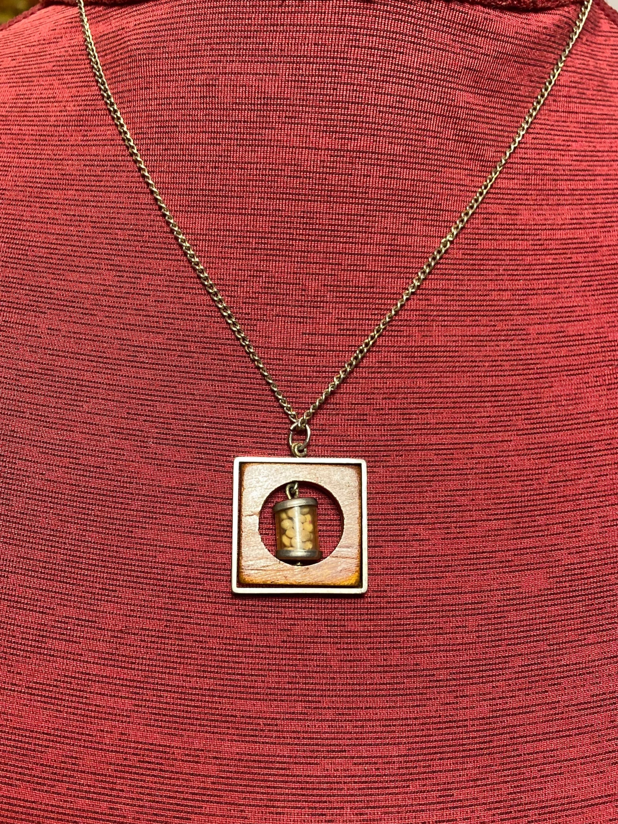 Vintage necklace with pendant containing small mustard seed bottle inside a circular opening inside a piece of wood encased in a metal frame hanging on a 19 inch chain