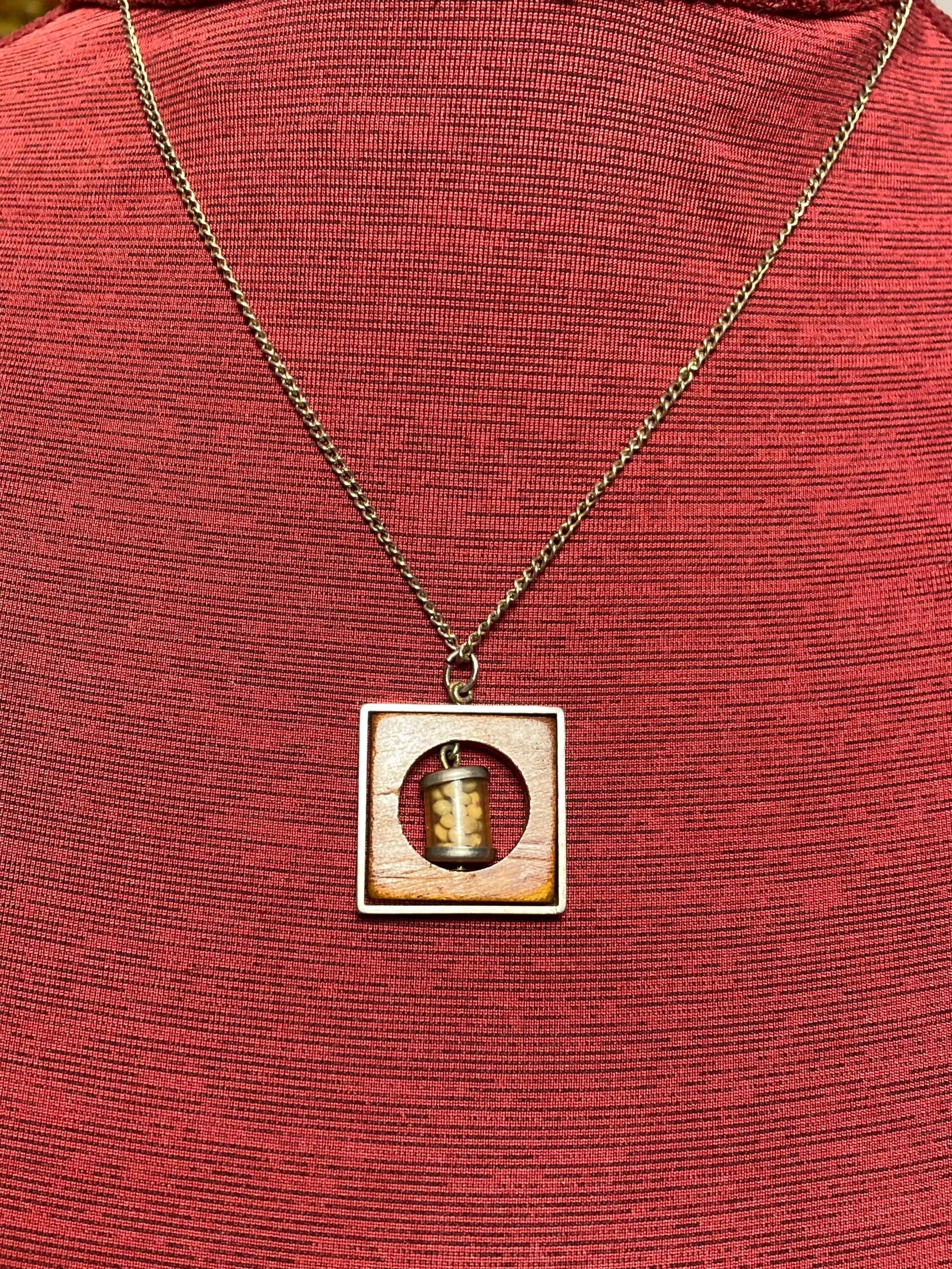 Vintage necklace with pendant containing small mustard seed bottle inside a circular opening inside a piece of wood encased in a metal frame hanging on a 19 inch chain