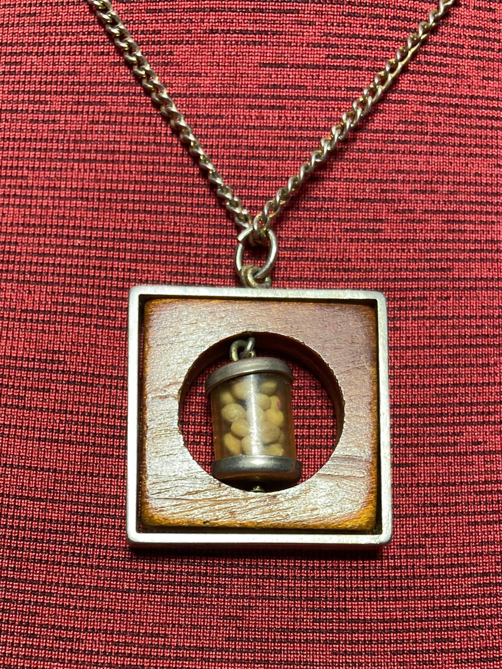 Vintage necklace with pendant containing small mustard seed bottle inside a circular opening inside a piece of wood encased in a metal frame hanging on a 19 inch chain