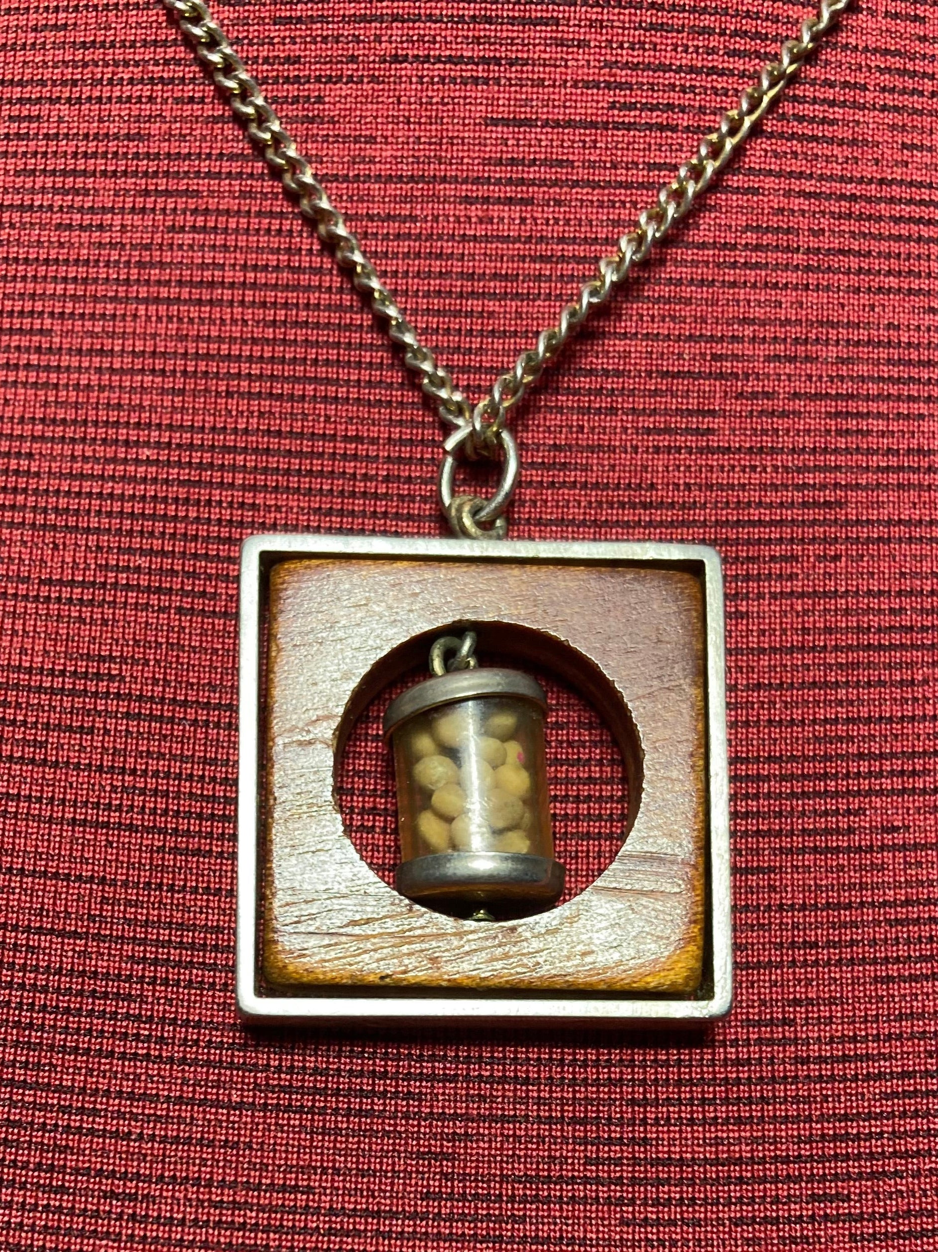 Vintage necklace with pendant containing small mustard seed bottle inside a circular opening inside a piece of wood encased in a metal frame hanging on a 19 inch chain