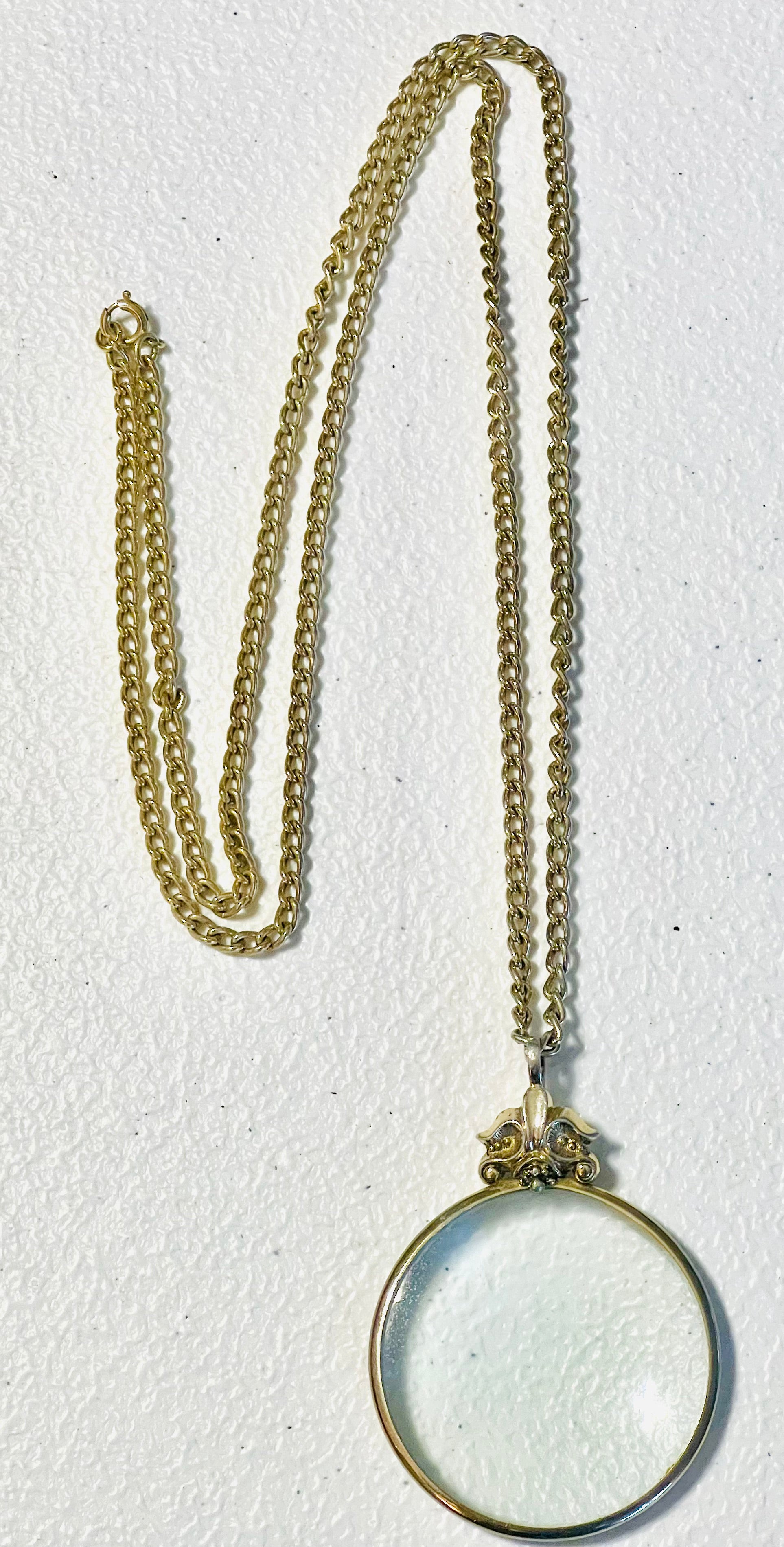 Vintage 1976 Avon magnifying glass pendant necklace with Fleur de Lis design and 28 inch serpentine gold tone chain.