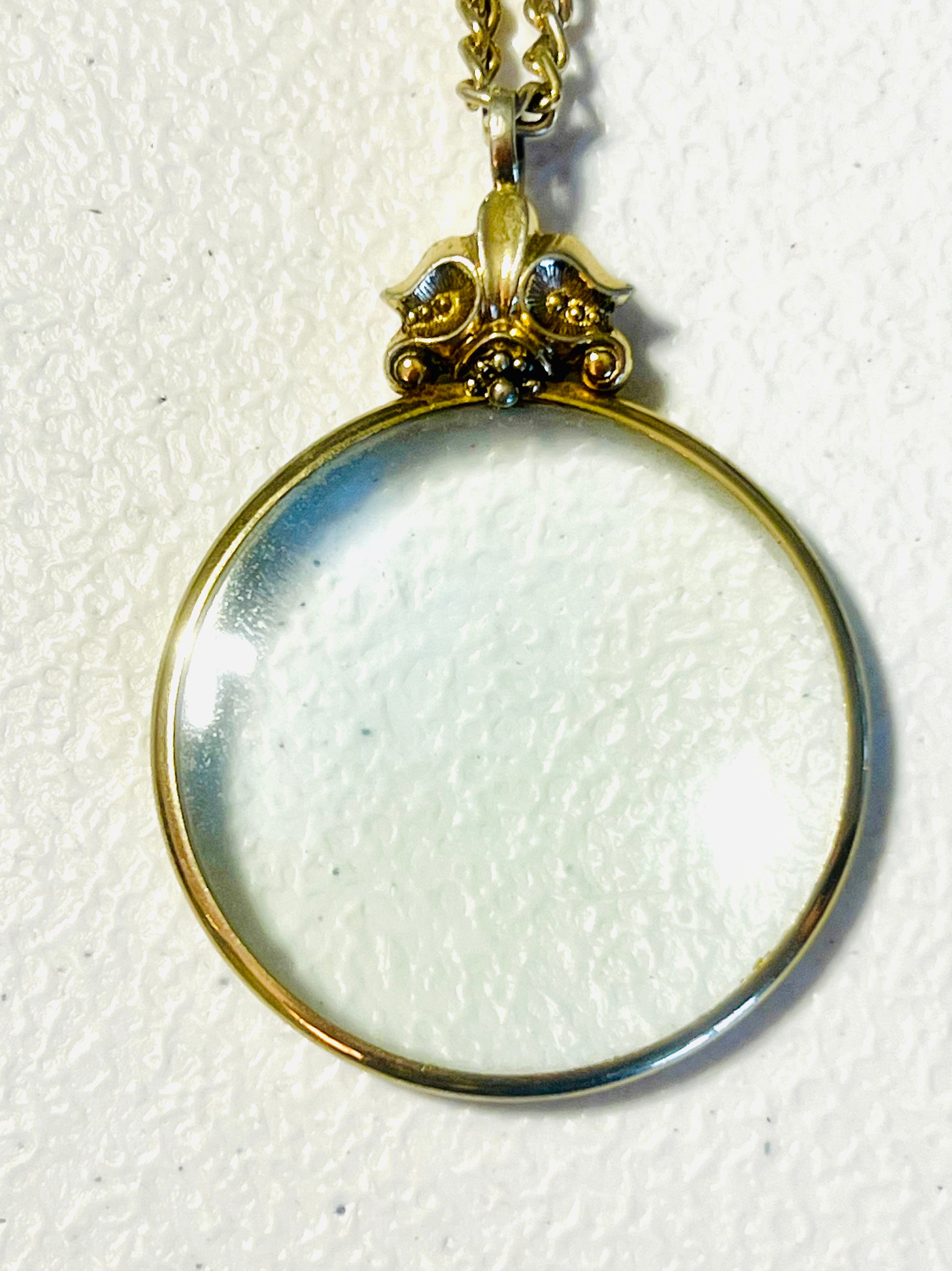 Vintage 1976 Avon magnifying glass pendant necklace with Fleur de Lis design and 28 inch serpentine gold tone chain.